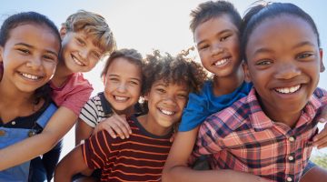 Six pre-teen friends piggybacking in a park, close up portrait